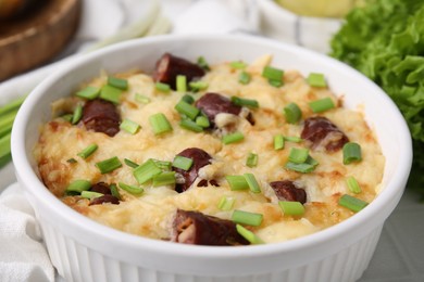 Photo of Tasty sausage casserole with green onion in baking dish on white table, closeup