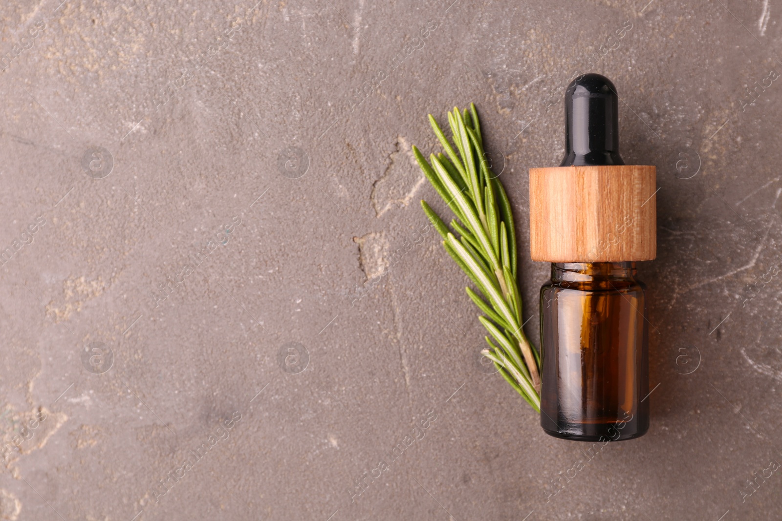 Photo of Essential oil in bottle and rosemary on grey table, top view. Space for text