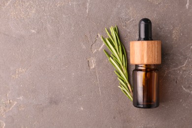 Essential oil in bottle and rosemary on grey table, top view. Space for text