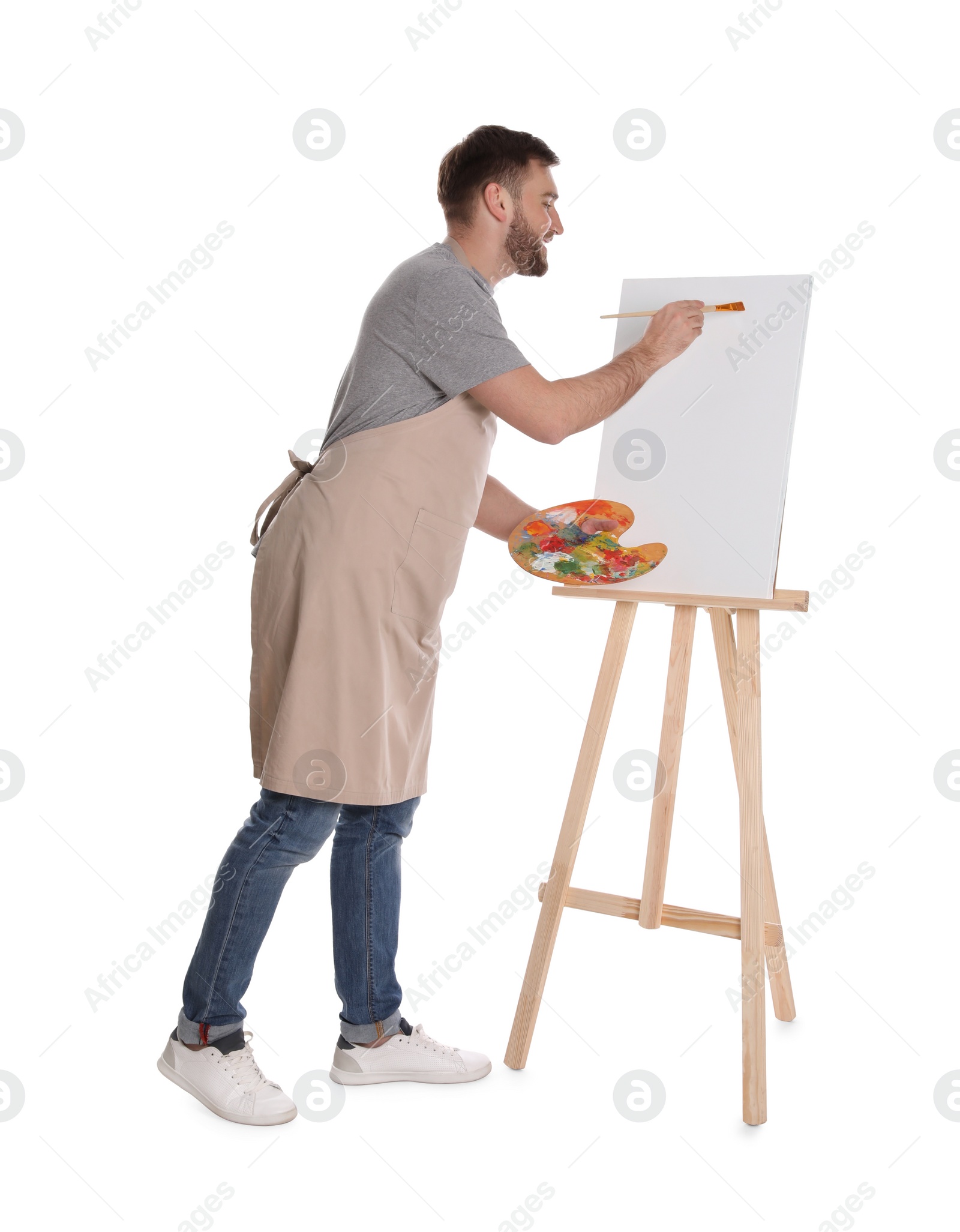 Photo of Man painting with brush on easel against white background. Young artist