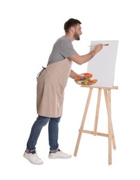 Man painting with brush on easel against white background. Young artist