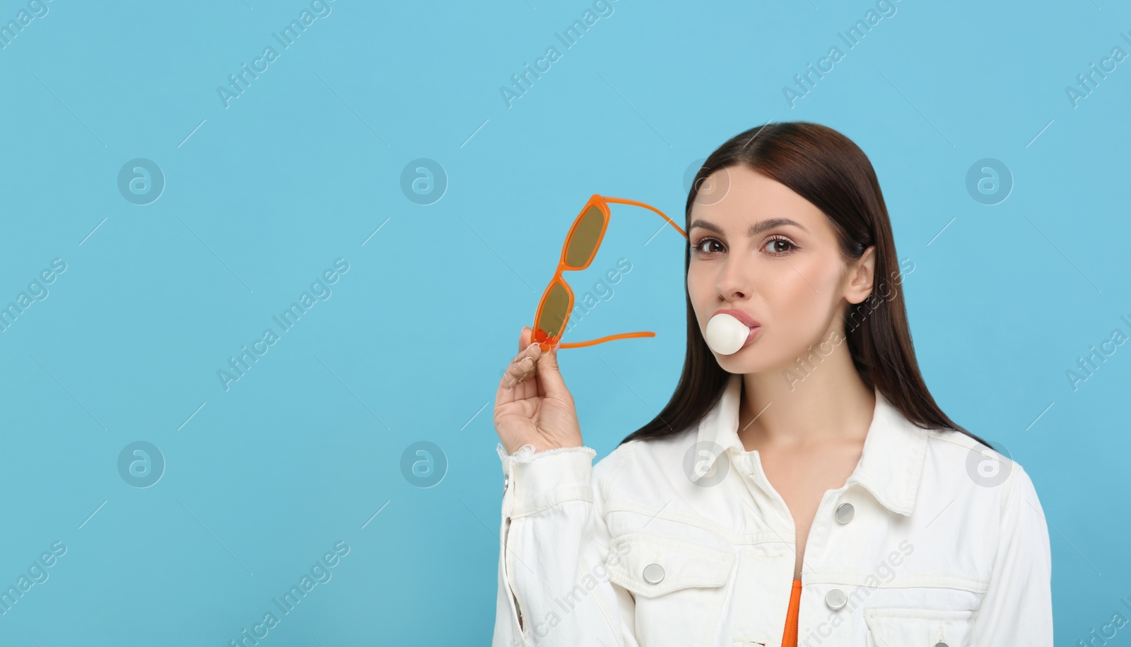 Photo of Beautiful woman with sunglasses blowing bubble gum on light blue background