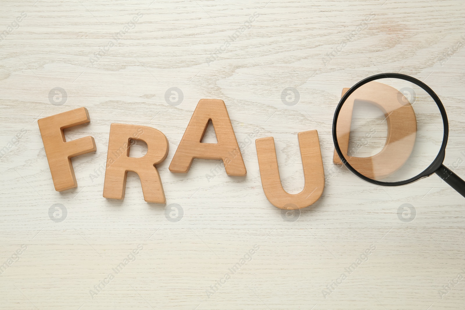 Photo of Word Fraud made of wooden letters under magnifying glass on white background, flat lay