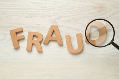 Photo of Word Fraud made of wooden letters under magnifying glass on white background, flat lay