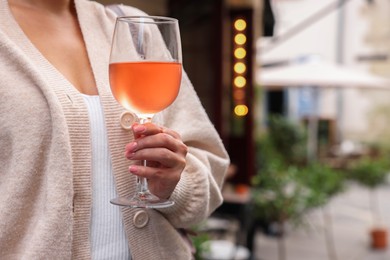 Photo of Woman holding glass of rose wine outdoors, closeup. Space for text