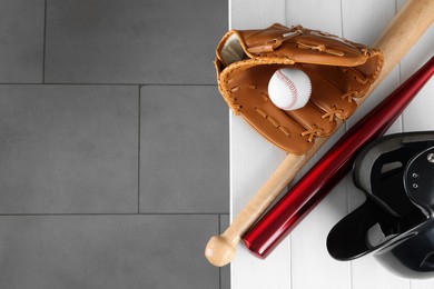 Photo of Baseball bats, batting helmet, leather glove and ball on white wooden bench indoors, top view. Space for text