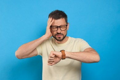 Photo of Man checking time on light blue background. Being late concept