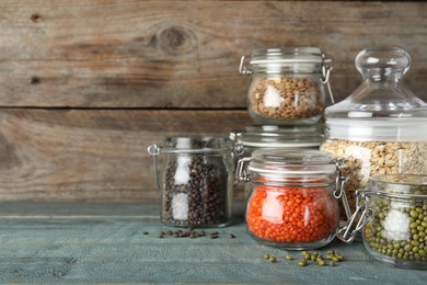 Different types of legumes and cereals in glass jars on blue wooden table, space for text. Organic grains
