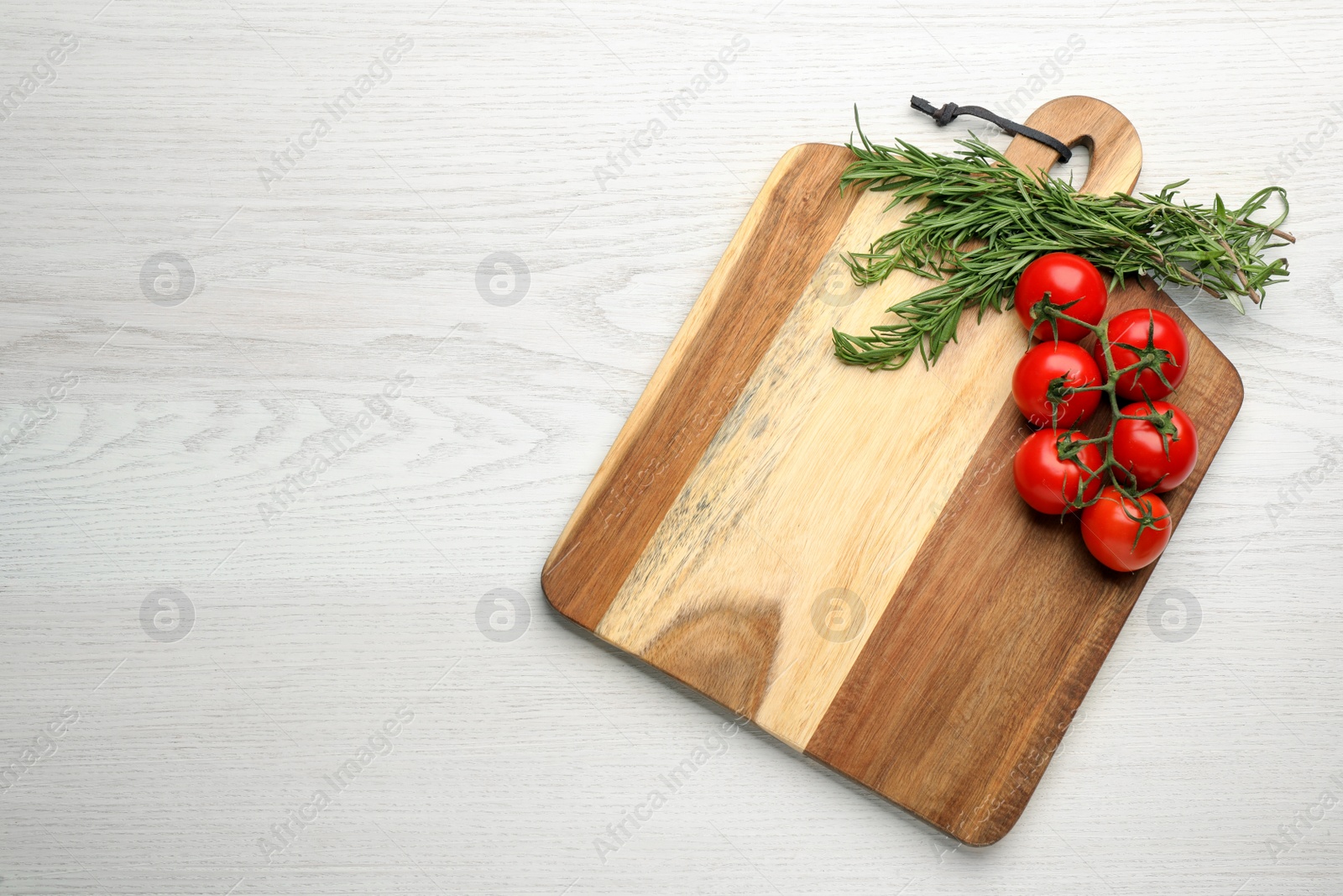 Photo of Cutting board, tomatoes and rosemary on white wooden table, top view with space for text. Cooking utensil