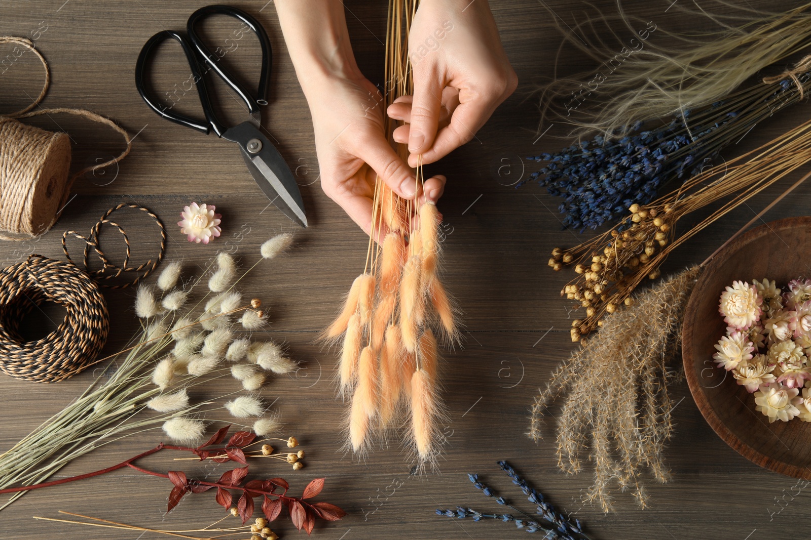 Photo of Florist making bouquet of dried flowers at wooden table, top view