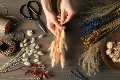 Photo of Florist making bouquet of dried flowers at wooden table, top view