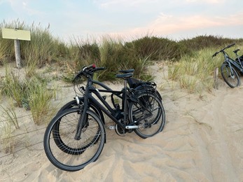 Three modern bicycles parked on sand outdoors