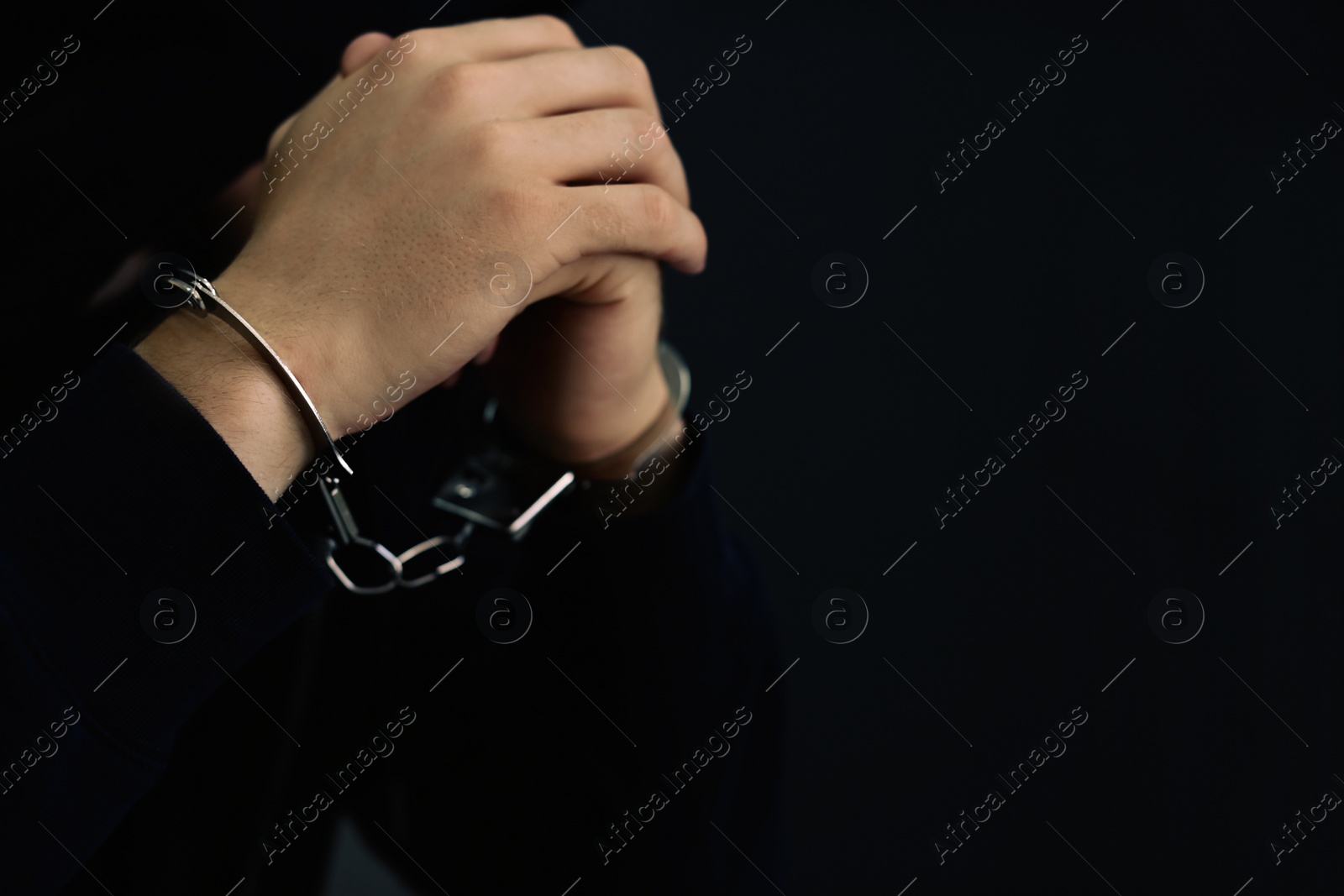 Photo of Man detained in handcuffs against dark background, space for text. Criminal law