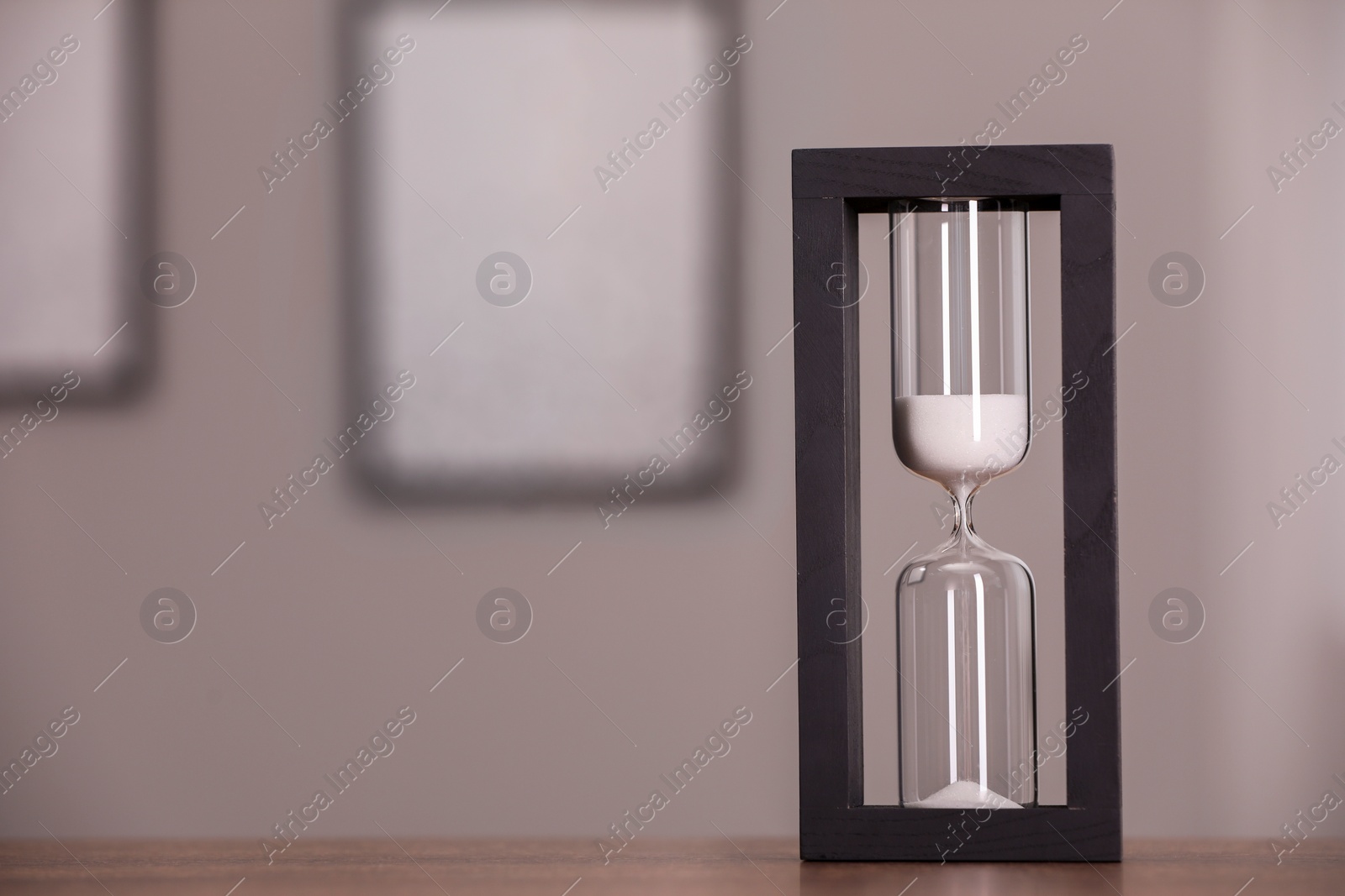 Photo of Hourglass with flowing sand on table against blurred background. Space for text