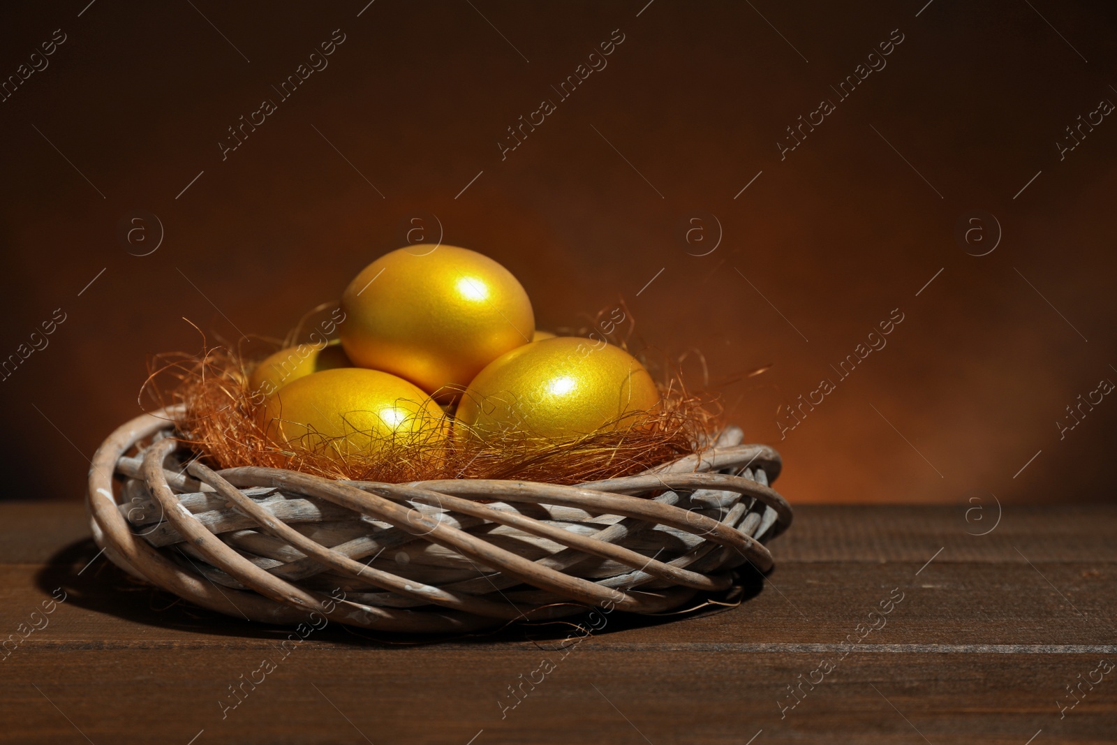 Photo of Shiny golden eggs in nest on wooden table, space for text