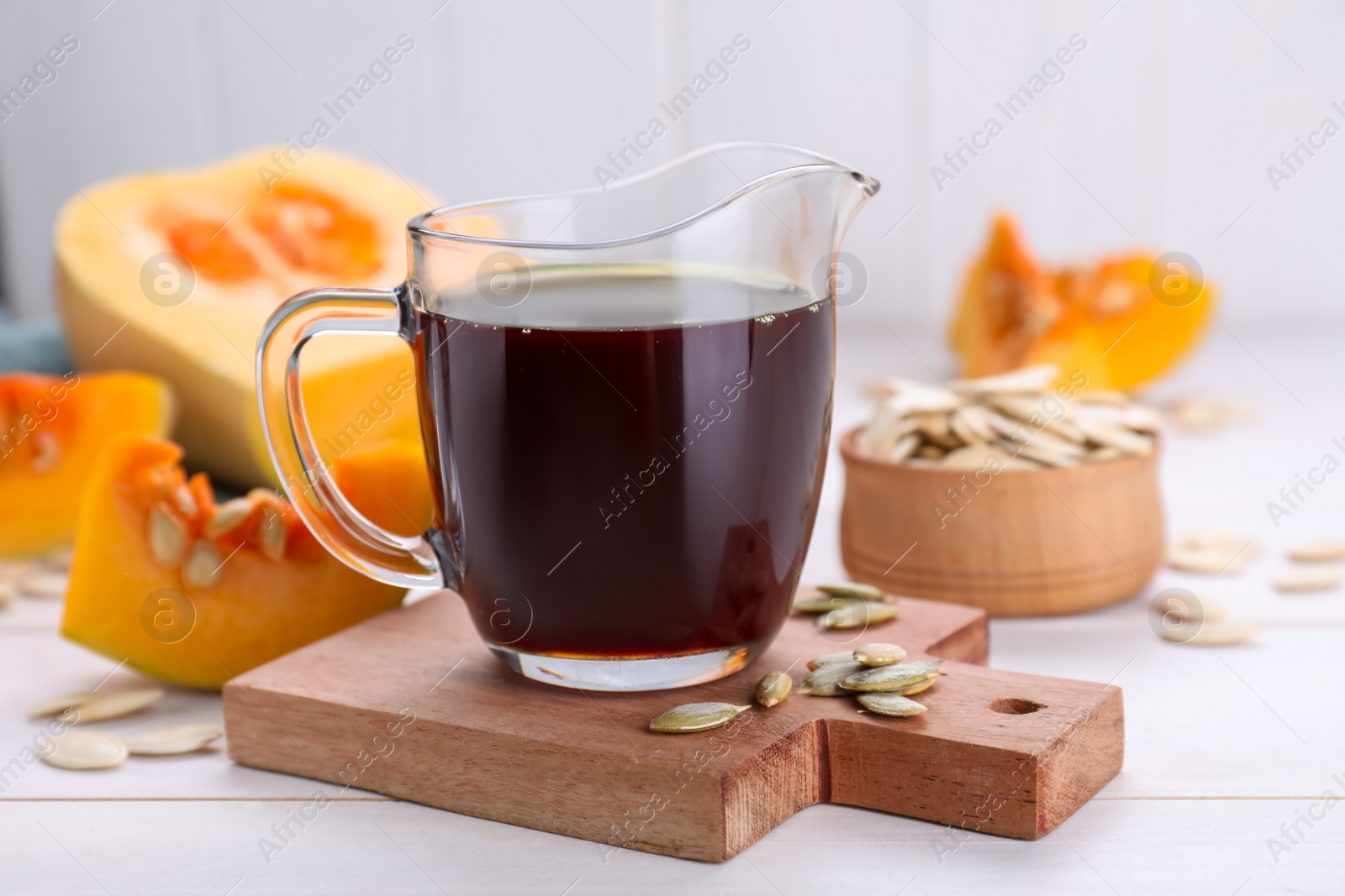 Photo of Fresh pumpkin seed oil in glass pitcher on white wooden table