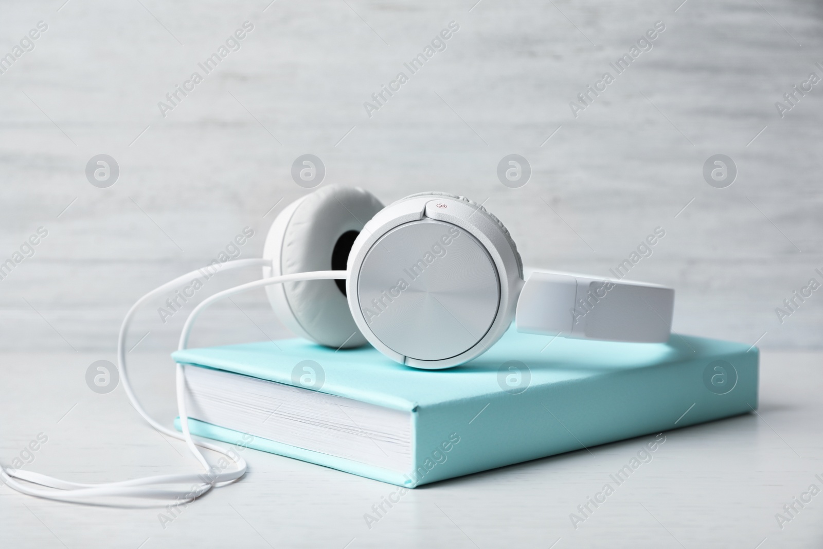 Photo of Modern headphones with hardcover book on wooden table