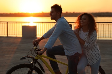 Young couple riding bicycle on city waterfront at sunset