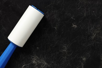 Photo of Lint roller and pet hair on black fabric, top view. Space for text