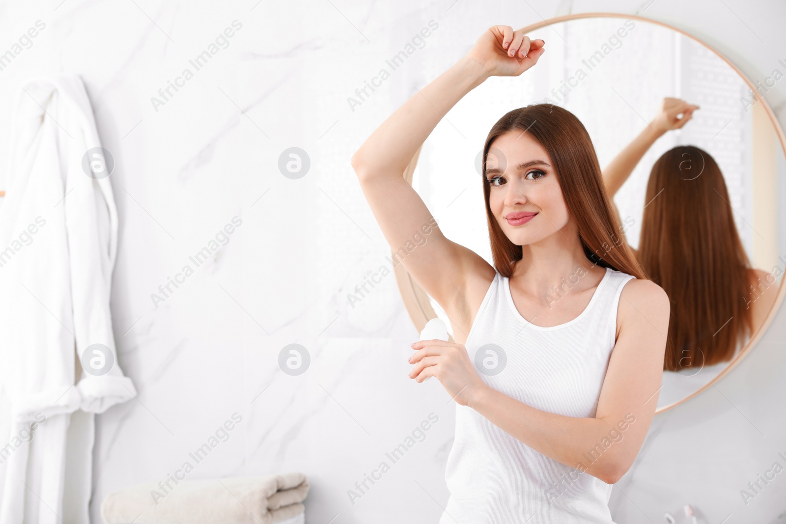 Photo of Beautiful young woman applying deodorant in bathroom. Space for text