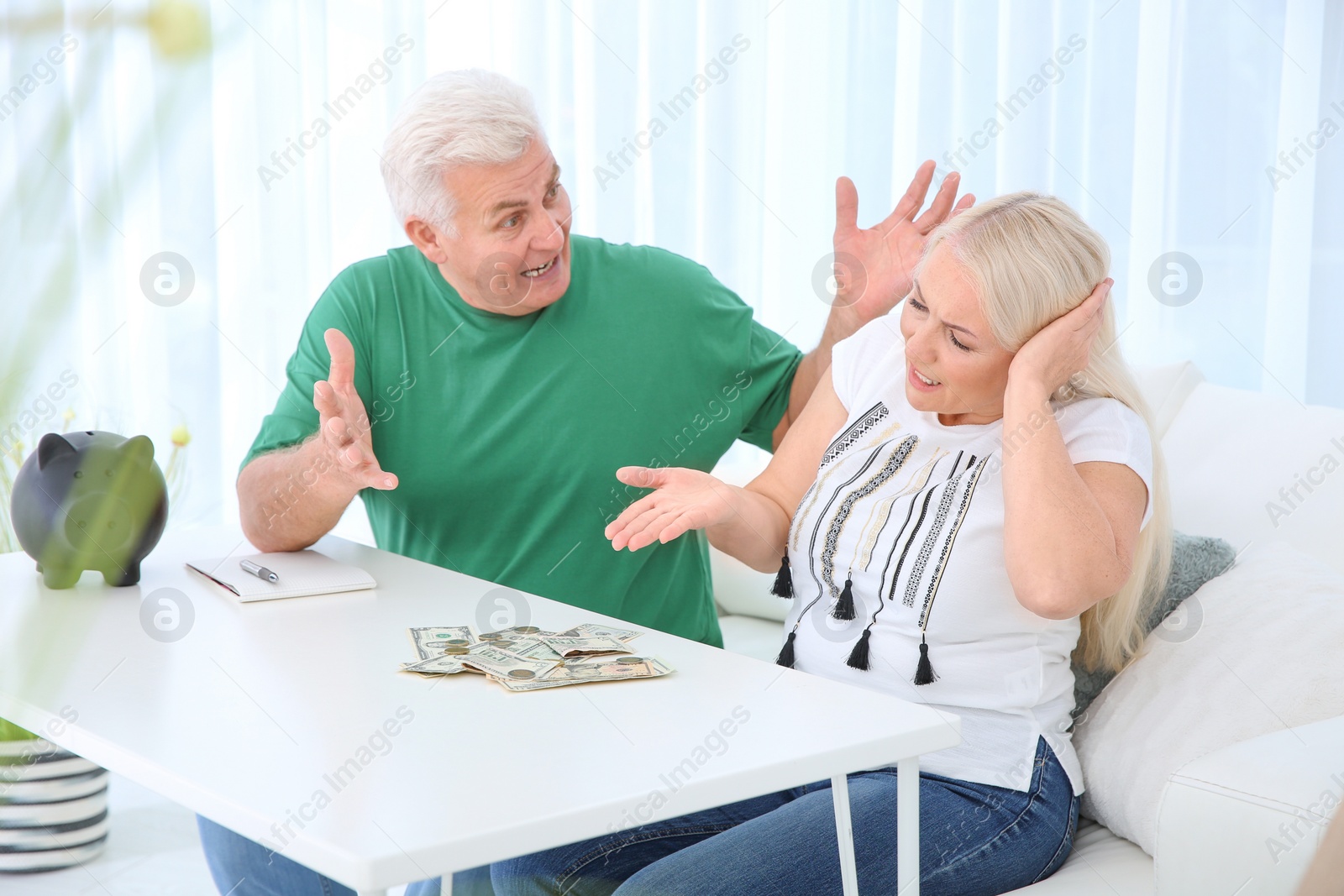 Photo of Mature couple with money and piggy bank having argument at table