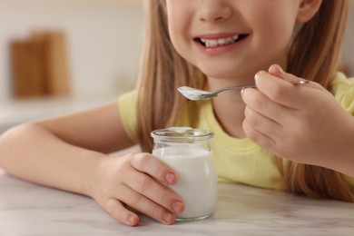 Photo of Cute little girl with tasty yogurt at white marble table indoors, closeup