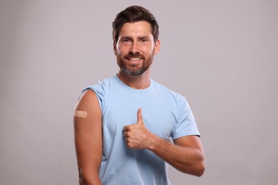 Photo of Man with sticking plaster on arm after vaccination showing thumbs up against light grey background