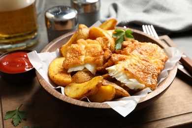 Photo of Wooden plate with British traditional fish and potato chips on table