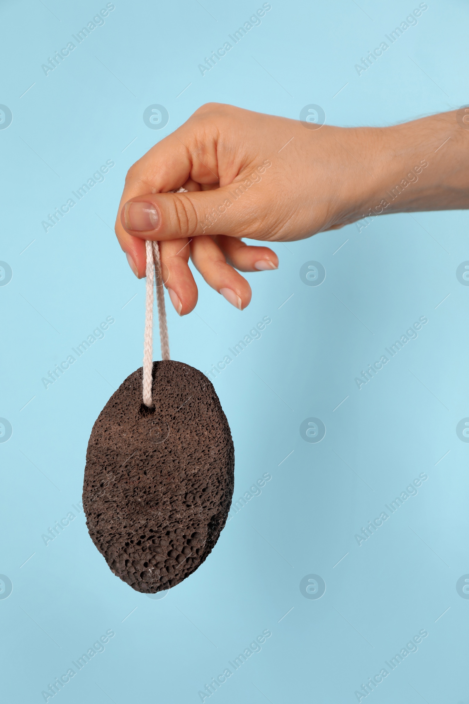 Photo of Woman holding pumice stone on light blue background, closeup