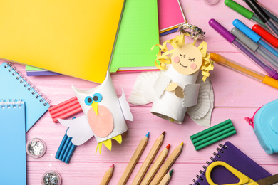 Photo of Owl and angel made of toilet paper hub among stationery on pink wooden table, flat lay