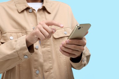 Young man sending message via smartphone on light blue background, closeup