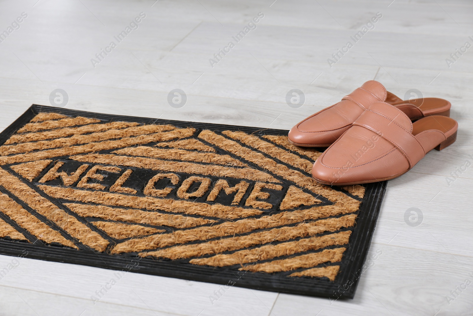 Photo of Door mat with word WELCOME and shoes on floor