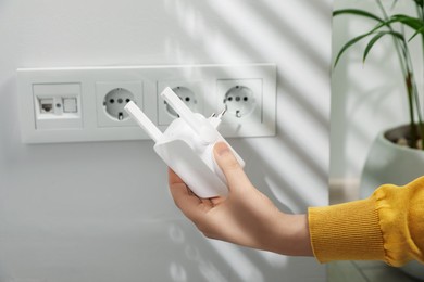 Woman holding wireless Wi-Fi repeater indoors, closeup