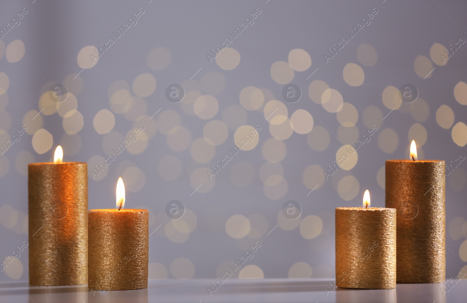 Photo of Burning gold candles on table against blurred lights. Space for text