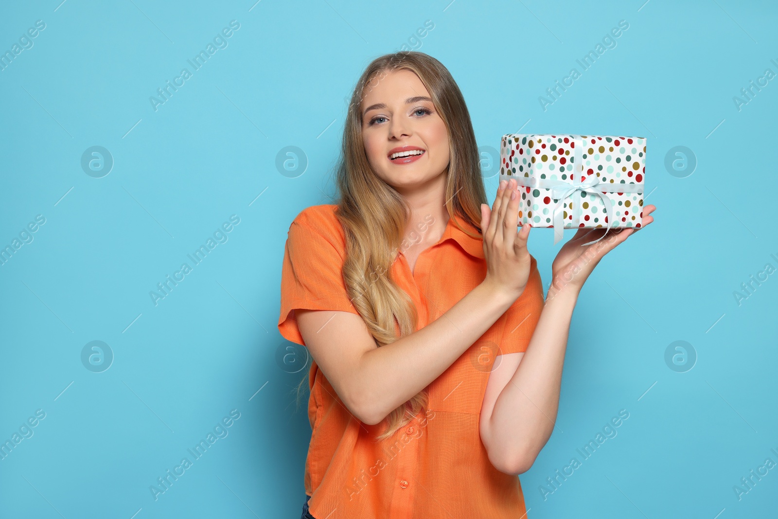 Photo of Beautiful young woman holding colorful gift box on light blue background