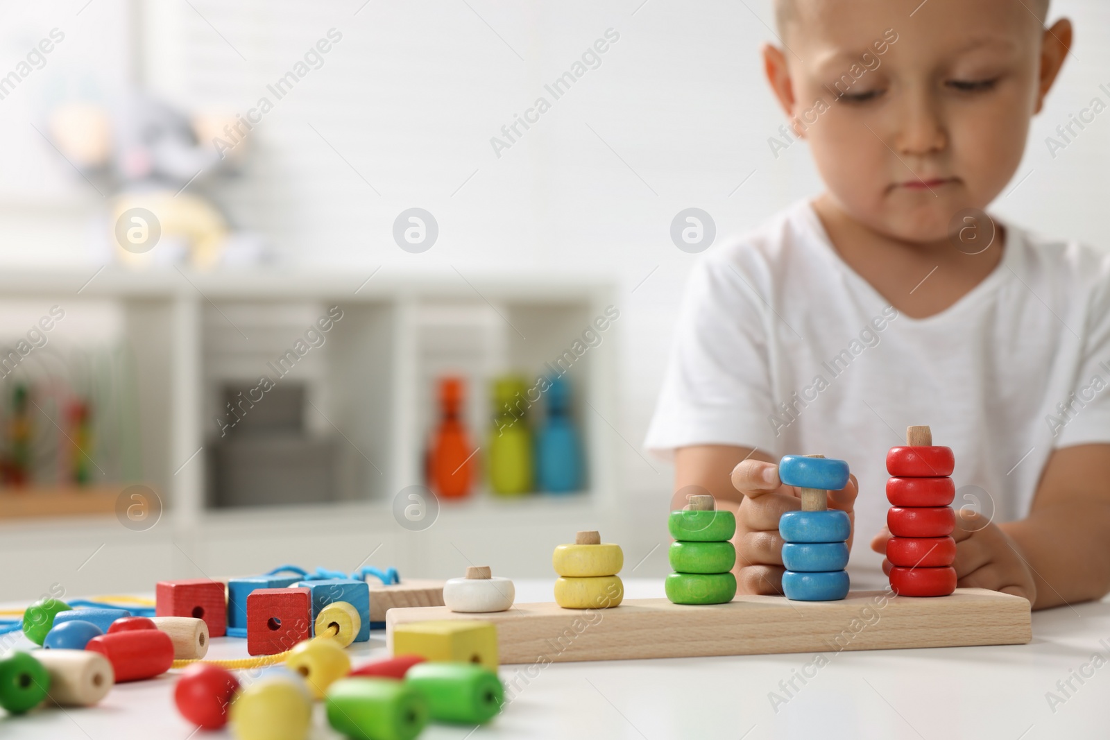 Photo of Motor skills development. Little boy playing with stacking and counting game at table indoors, closeup