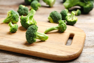 Photo of Wooden board with fresh broccoli florets on table, closeup