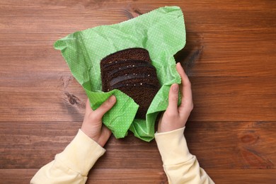 Photo of Woman packing slices of rye bread into beeswax food wrap at wooden table, top view