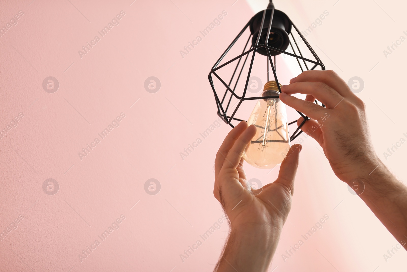 Photo of Man changing light bulb in lamp on color background. Space for text