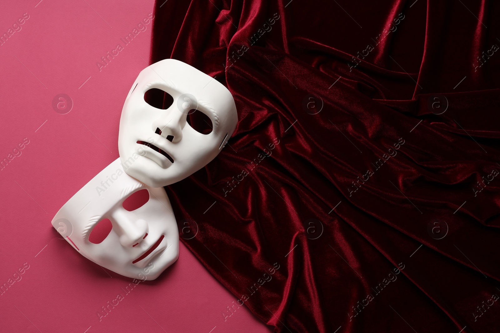Photo of Theater arts. White masks and red fabric on pink background, top view