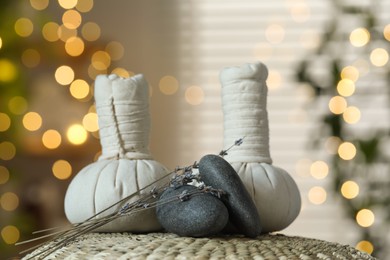 Photo of Spa composition. Herbal bags, stones and dry lavender flowers on wicker mat indoors, bokeh effect