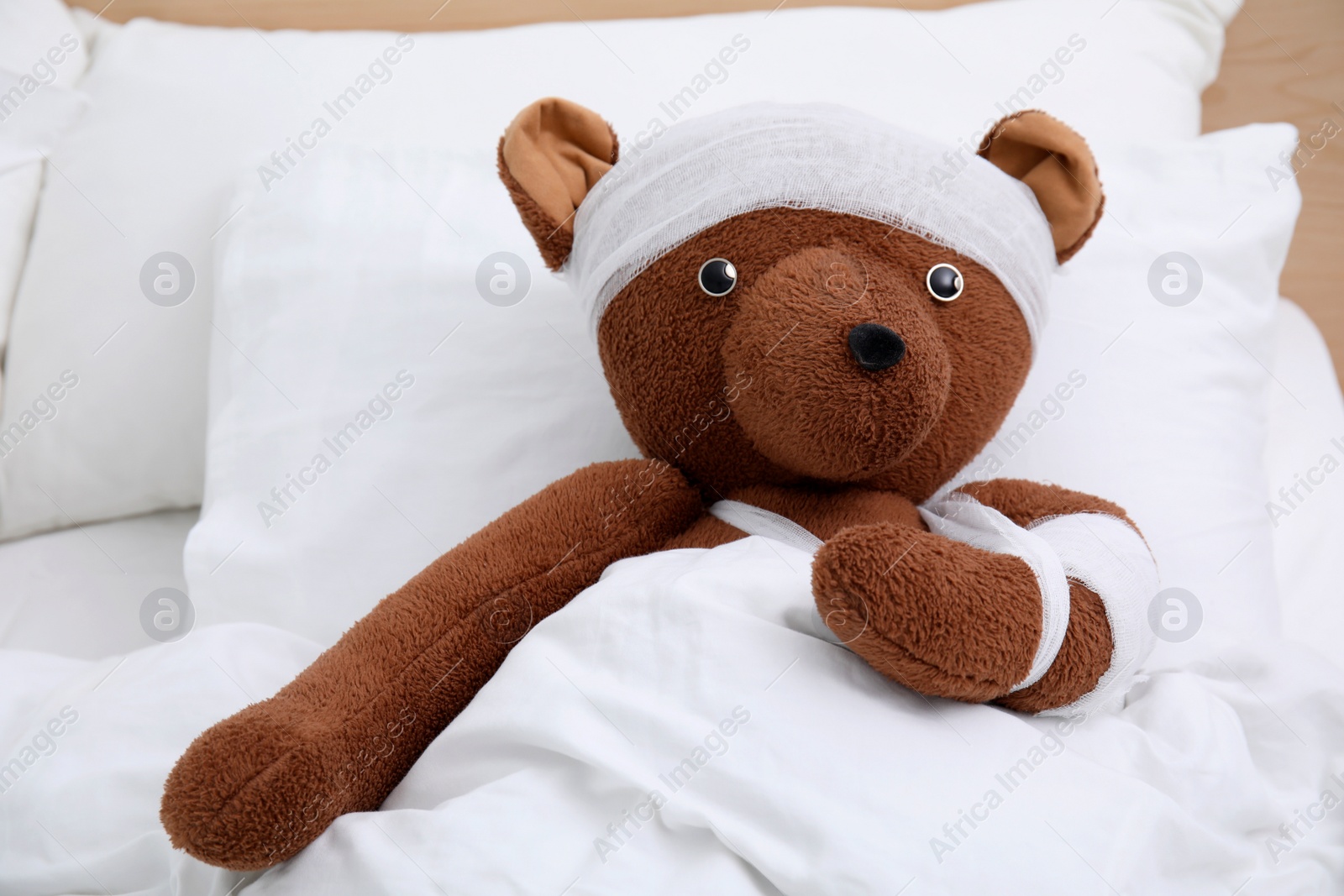 Photo of Toy bear with bandages lying in bed