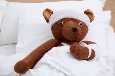 Photo of Toy bear with bandages lying in bed