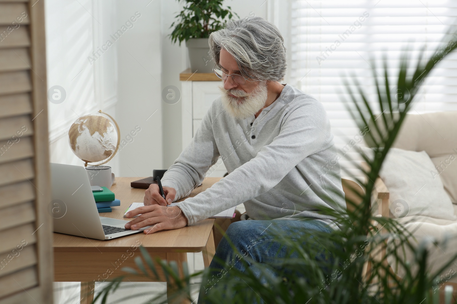 Photo of Middle aged man with laptop and notebook learning at table indoors