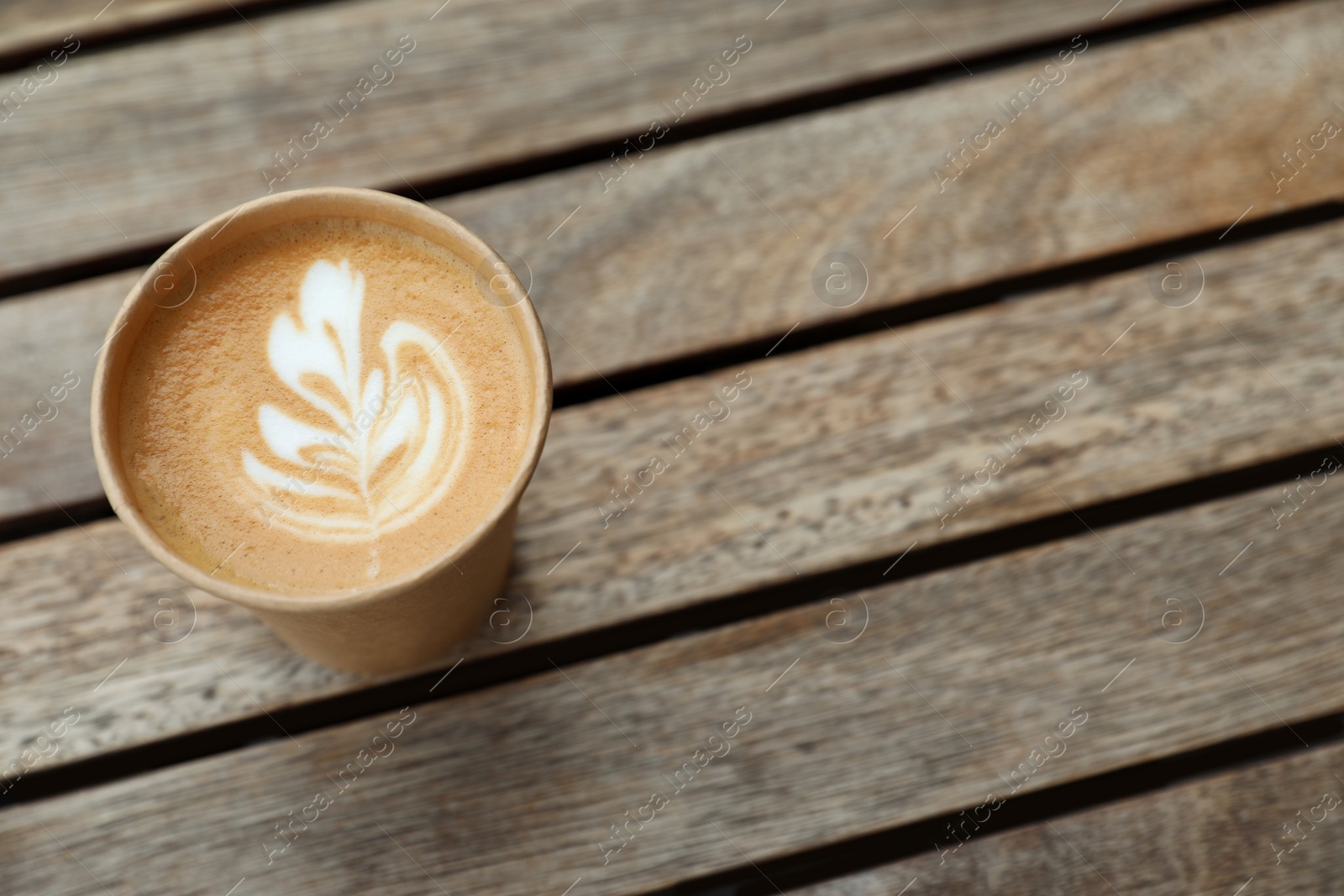 Photo of Takeaway paper cup with coffee on wooden table, above view. Space for text