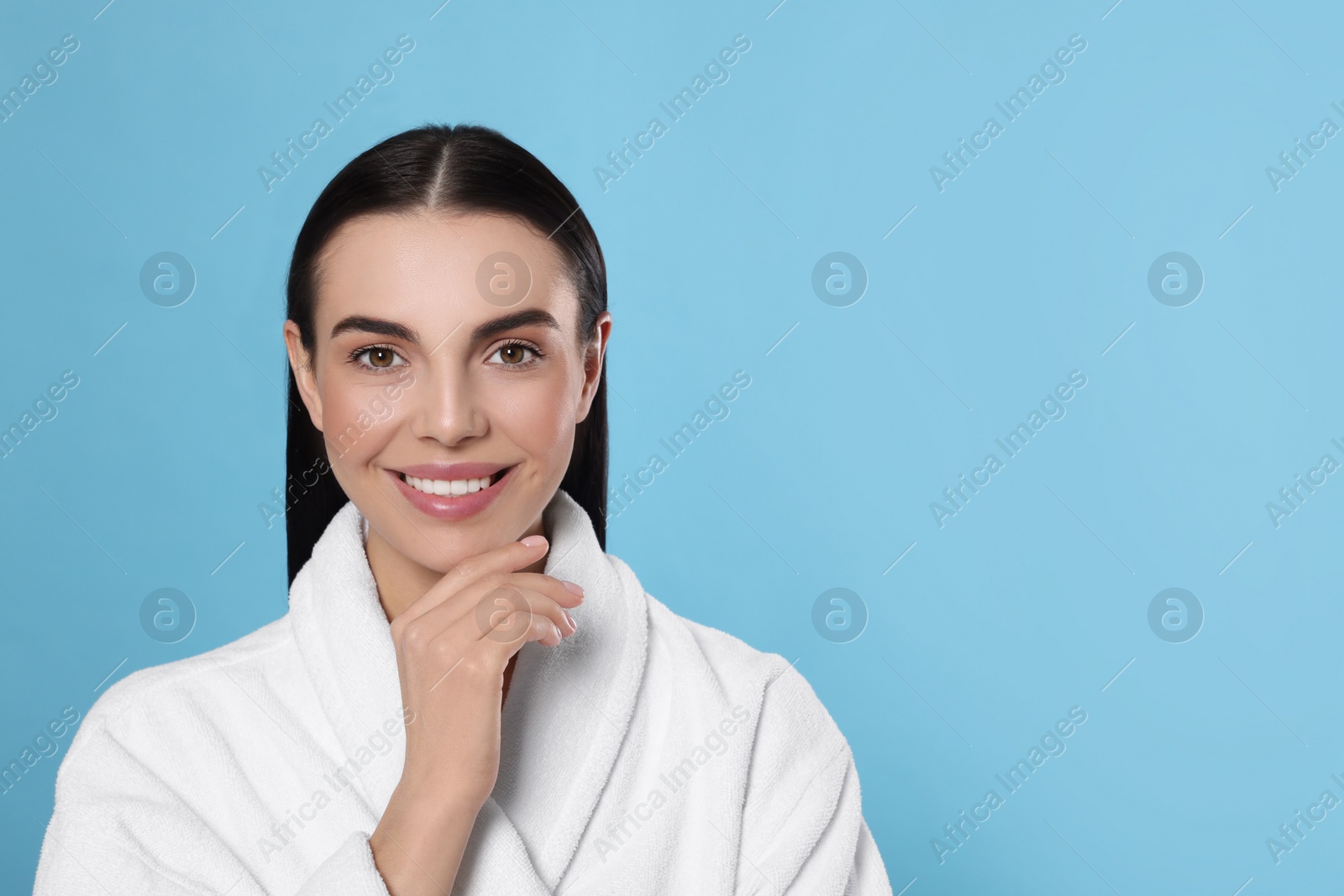 Photo of Portrait of attractive young woman in bathrobe on light blue background, space for text. Spa treatment