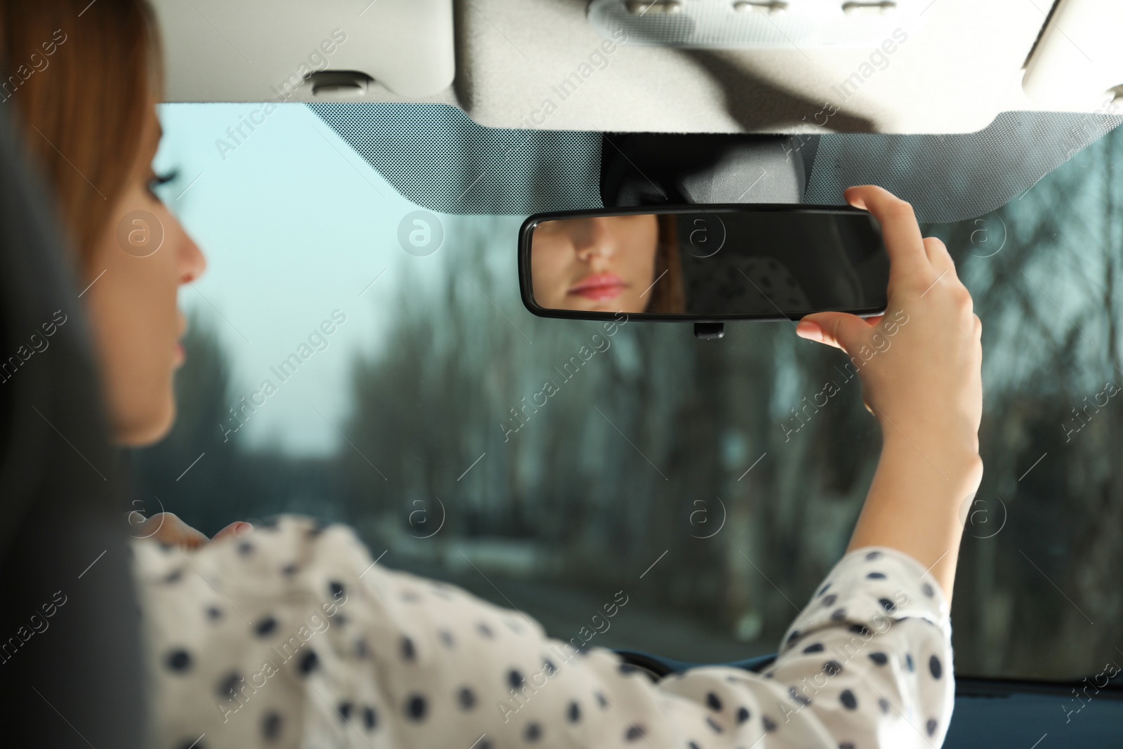 Photo of Young woman adjusting rear view mirror in car, closeup