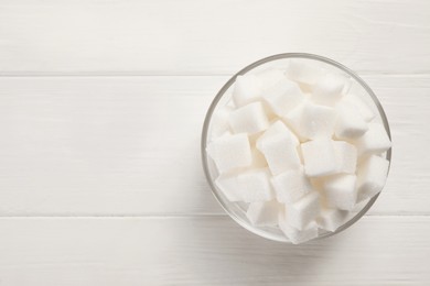 Photo of Bowl with sugar cubes on white table, top view. Space for text