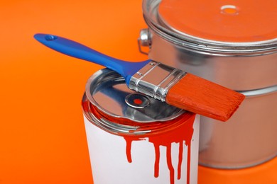 Photo of Cans of orange paint and brush on color background, closeup