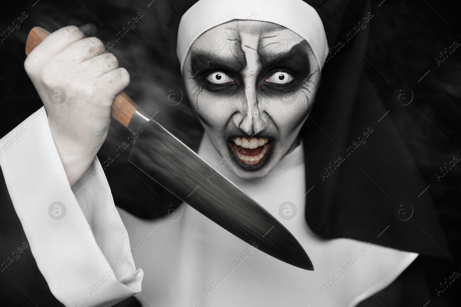 Photo of Scary devilish nun with knife on black background. Halloween party look